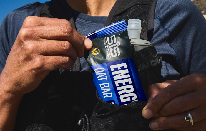 Un athlète portant un gilet et tenant une barre SiS Energy Oat Bar à la myrtille