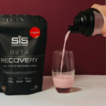 BETA Recovery Shake wird in ein Glas gegossen, daneben liegt eine Tüte BETA Recovery