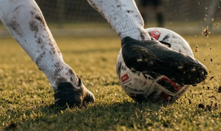 Un calciatore ricoperto di fango che calcia un pallone
