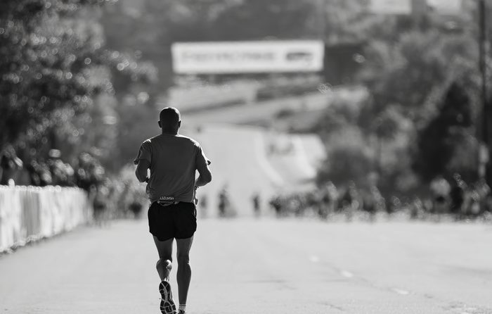 Black and white photo of a lone runner viewed from behind on an open city road