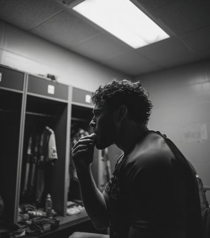 Athlete eating a quick snack in a dimly lit changing room, profile view