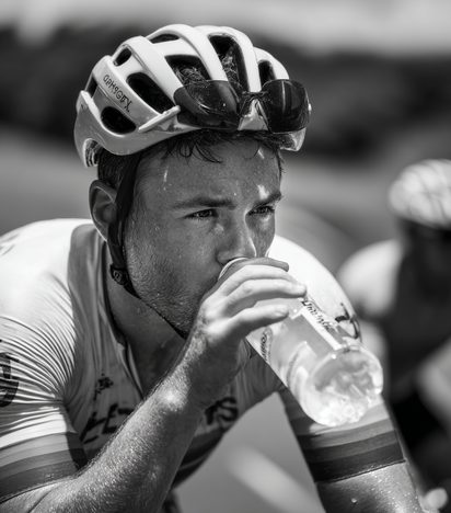 Close-up of a cyclist drinking from a water bottle mid-ride, sweat visible on his face