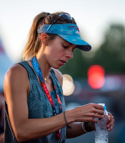 Female runner holding a water bottle while running alone on an open race road