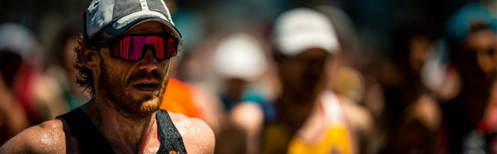 Primer plano de un corredor empapado en sudor, con gorra y gafas de sol, que se abre paso en una carrera bajo un calor abrasador