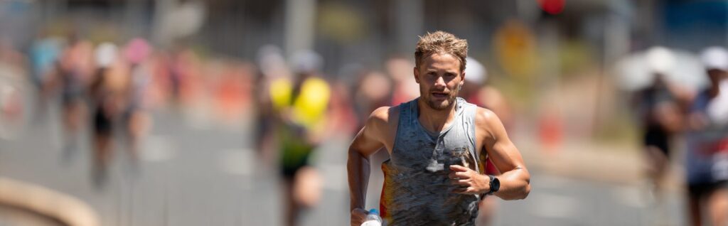 Runner with a heavily sweat-stained shirt gripping a water bottle mid-race