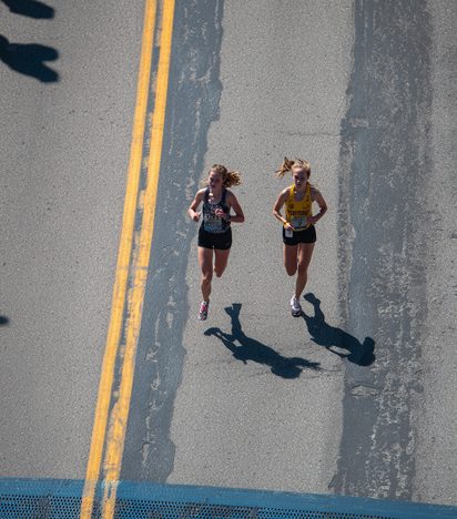 Two male marathon runners captured mid-stride side by side, backlit by low sun