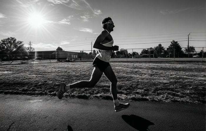 Photo en noir et blanc d'un coureur qui garde une foulée assurée face à un soleil bas