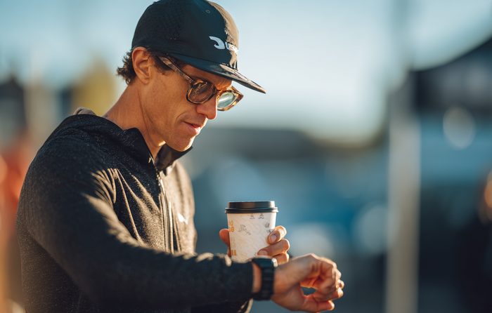 Un sportif qui regarde sa montre tout en tenant une tasse de café à l'extérieur