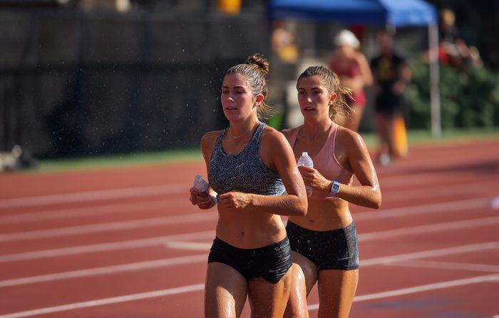 two athletes jogging on a track, sweat-drenched, in harsh midday light.