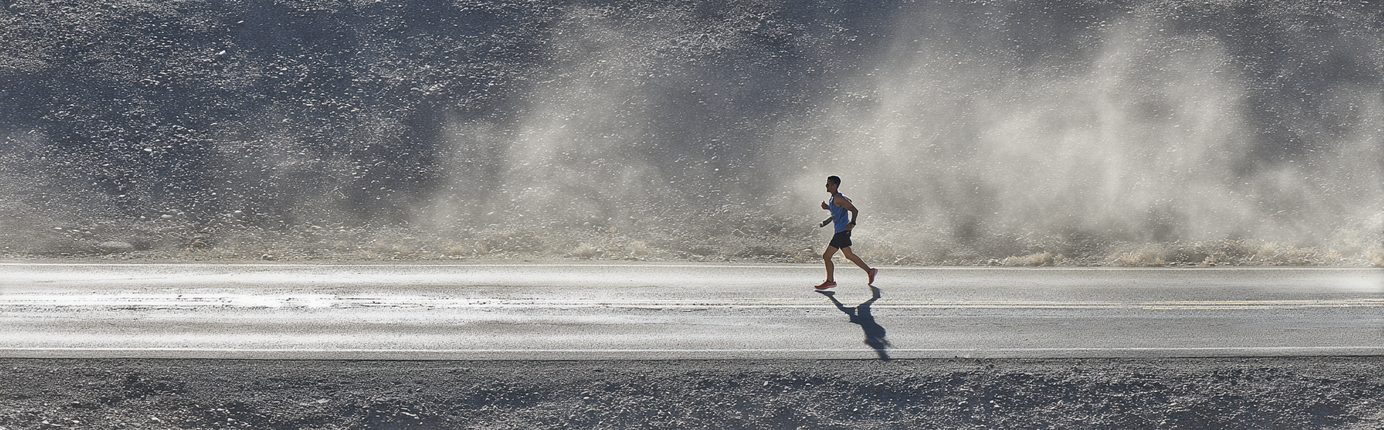 Black and white photo of a runner moving through visible heat haze rising off a desert road.