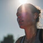 close-up of a sweating runner's face lit by low sun, earbuds visible.