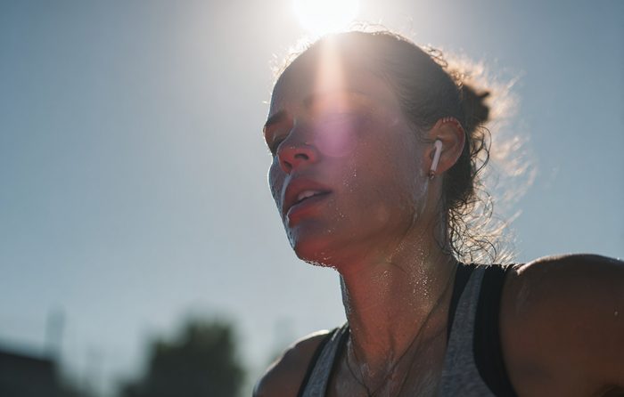 Gros plan sur le visage d'un coureur en sueur, éclairé par le soleil bas, avec ses écouteurs bien visibles.