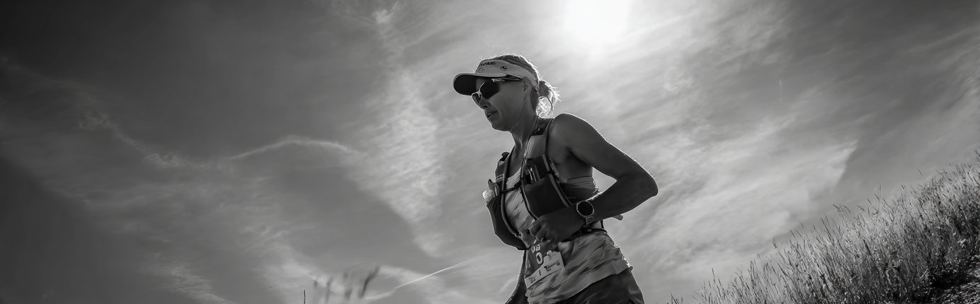 Photo en noir et blanc d'un coureur de trail à contre-jour sous un soleil de plomb, portant un gilet d'hydratation